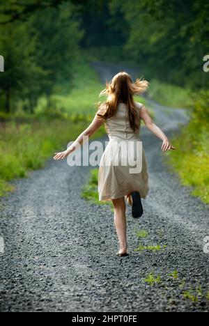 Young woman running up gravel country road, arms wide Stock Photo