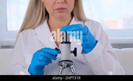 Female laboratory assistant analyzes samples using a microscope while working at a table in a laboratory, doing research Stock Photo