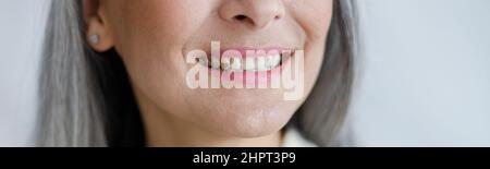 Positive mature lady smiles showing healthy teath on light background in studio closeup Stock Photo
