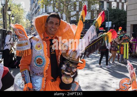 Man wearing a sumptuous white and orange Hispanic-style costume poses proudly holding a traditional Bolivian mask. Hispanic Day in Barcelona, Spain. Stock Photo