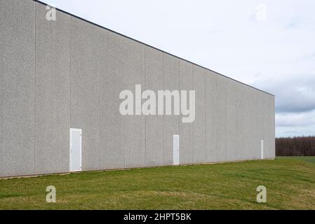 a warehouse building in light gray concrete against the blue sky and a lawn in the foreground , Frederikssund, Denmark, February 22, 2022 Stock Photo