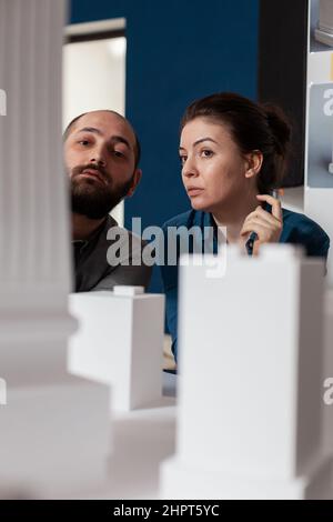 Professional architects team inspecting skyscraper white foam model design in architectural modern office. Project engineers colleagues lookin inspired in front of 3d residential maquette. Stock Photo