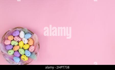 Creative pastel pink copy space background with wooden basket and vibrant colored eggs for Easter holidays. Spring Flat lay concept Stock Photo
