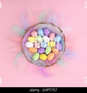 Creative Easter pastel bright pink background with rainbow feathers and colored eggs in wooden basket. Flat lay minimal. Spring holidays concept Stock Photo