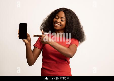 Online Offer. Cheerful Black Female Pointing On Blank Smartphone In Hand Stock Photo