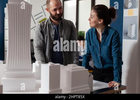 Architects doing teamwork looking at each other discussing blueprints in modern architecture office. Team of two architects colleagues working together at urban planning project. Stock Photo
