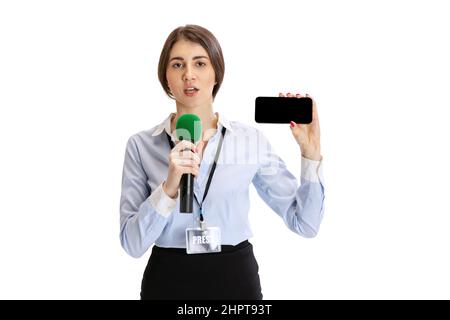 Portrait of young serious girl, correspondent showing phone screen isolated on white studio background. Concept of social media, press, news Stock Photo