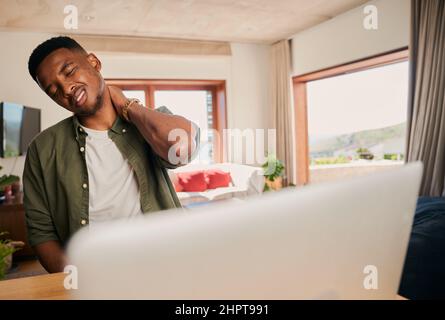 Young adult black male holding his neck in pain. Remote working on laptop from home in modern kitchen. Stock Photo