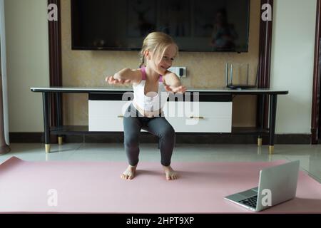 Cute little girl in sportswear doing fitness exercises at home. Distant  training with personal trainer, social distance or self-isolation, online  Stock Photo - Alamy