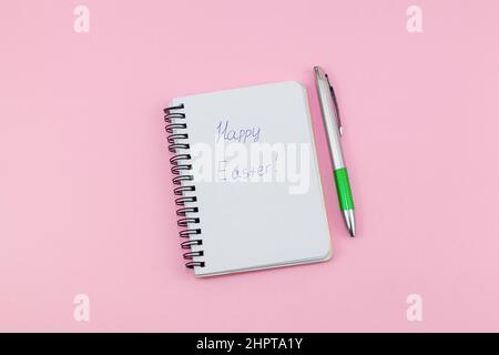 Notepad and pen on pink background. Lettering Happy Easter. Notebook for ideas message, list and inspiration. Top view, flat lay with copy space. Mock Stock Photo
