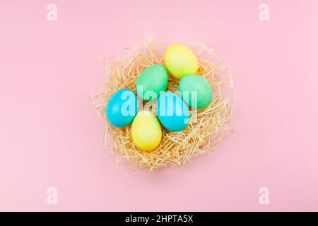 Easter eggs painted in pastel colors in hay nest against a pink background, copyspace for Happy Easter text Stock Photo