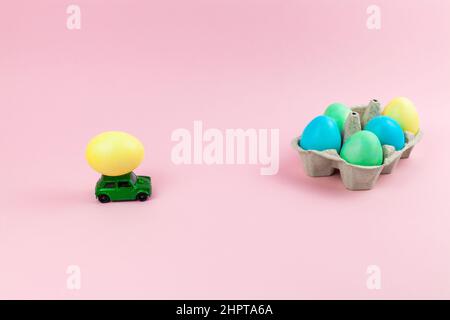 Toy green car with Easter egg on the roof. Easter card with space for text on a pink background. Easter grocery delivery Stock Photo