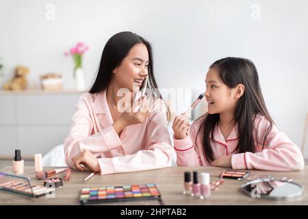 Glad happy japanese teen girl and young woman in pajamas at table with cosmetics apply makeup Stock Photo