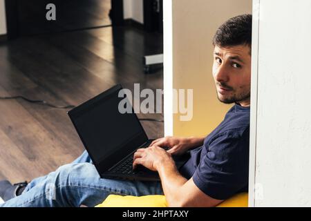 Handsome bearded man working on laptop and sitting on yellow bean bag soft armchair in modern office Stock Photo