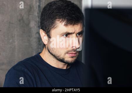 Handsome serious bearded man sitting at the office desk, working and looking at computer screen against concrete wall in modern office Stock Photo