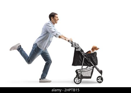 Full length profile shot of a casual young man pushing a dog stroller and running isolated on white background Stock Photo