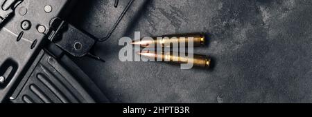 Two bullets and Kalashnikov assault rifle on gray concrete background banner, top view panoramic web header. Cartridge 7.62 caliber for ak 47. Wide sc Stock Photo