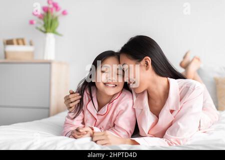 Satisfied happy millennial japanese lady and teen girl in pajamas with closed eyes lie on bed, enjoy relaxation Stock Photo