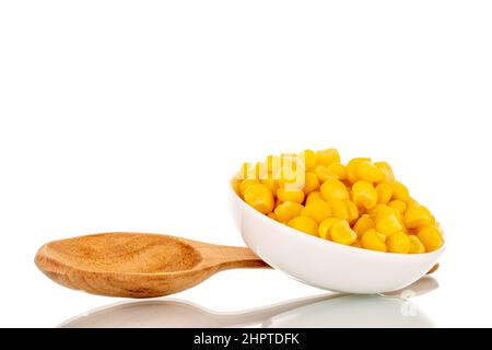 Bright yellow canned corn kernels in white ceramic saucer with wooden spoon, macro, isolated on white background. Stock Photo