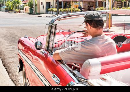 Man sitting in red vintage 1957 car on street of resort town Varadero, Cuba. Stock Photo