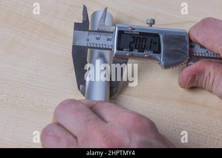 Close up view of hands man  measuring an aluminum pipe with an electronic calipers isolated on white background. Sweden. Stock Photo