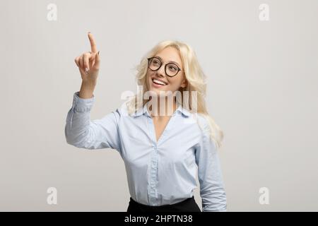 Happy female entrepreneur pushing button on virtual screen over light grey studio background, mockup for design Stock Photo