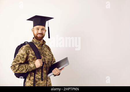 Happy military student in camouflage uniform and graduate cap standing on copy space background Stock Photo