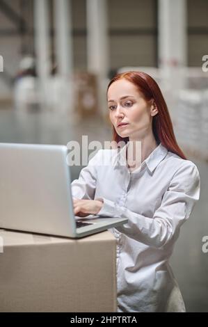 Woman working on laptop in industrial warehouse Stock Photo