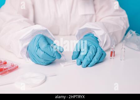 Doctor in medical PPE suit holds a Coronavirus antigen test of care testing. Lab performing rapid diagnostic test for antibodies to detect presence of Stock Photo