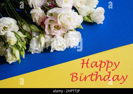 Stylish Birthday greeting card design. Text Happy Birthday on yellow background.White eustoma flowers is in envelope. Trendy flat lay. Stock Photo