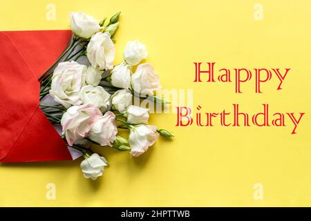 Stylish Birthday greeting card design. Text Happy Birthday on yellow background.White eustoma flowers is in envelope. Trendy flat lay. Stock Photo