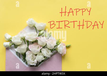Stylish Birthday greeting card design. Text Happy Birthday on yellow background.White eustoma flowers is in envelope. Trendy flat lay. Stock Photo