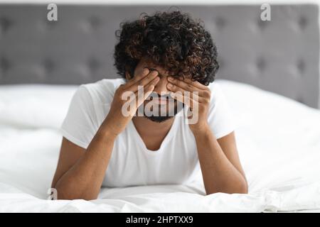 Upset guy laying on bed, rubbing his eyes Stock Photo