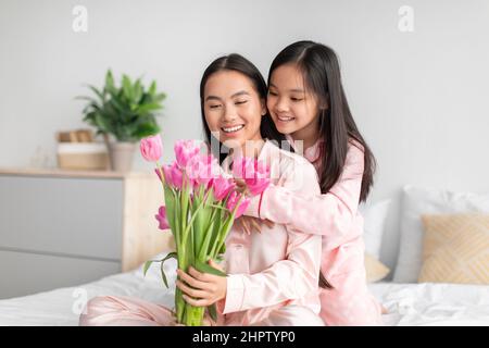 Glad happy japanese teenage girl hugging young woman in pajama, giving bouquet of tulips Stock Photo