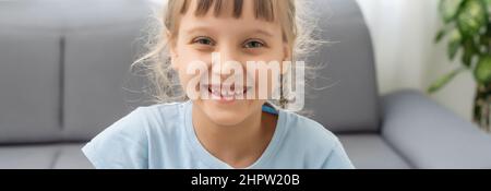 Adorable cute little vlogger looking at webcam, smiling child girl talking to camera making video call vlog communicating online sitting on couch at Stock Photo