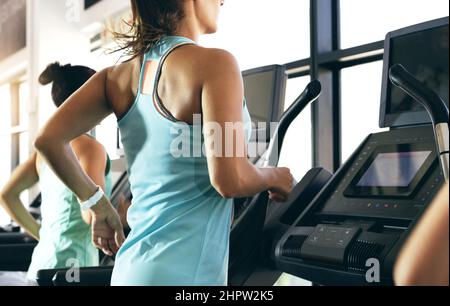 Getting into full flow. Rearview shot of two unrecognizable young women working out on treadmills in the gym. Stock Photo