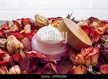 Pink color jar with velvety texture white handmade body butter cream, dry rose petals and puds background, copy space. Stock Photo