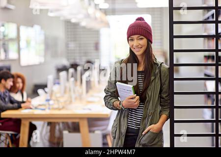 We live and learn. Portrait of a female student standing in a library holding a textbook. Stock Photo