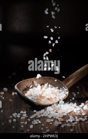 A falling of salt on a dark background, a spoonful of salt lies on top.  Coarse salt Stock Photo