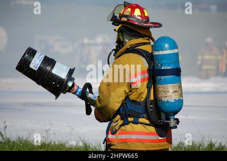 Firefighter in full turnout gear and self-contained breathing apparatus stands ready with foam nozzle Stock Photo