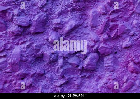 Violet painted relief wall with rough chaotic convex elements. Concrete wall covered uneven decorative stucco and painted bluish-purple paint. Stock Photo