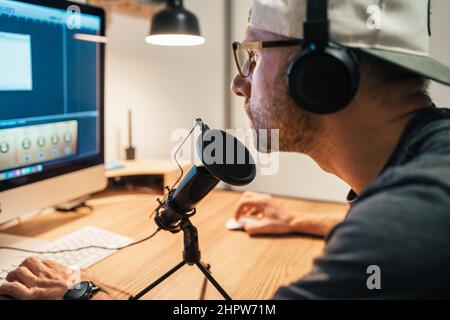 Middle-aged in headphones and baseball making video audio editing using a desktop computer with media edit software. Modern home sound and audio monta Stock Photo