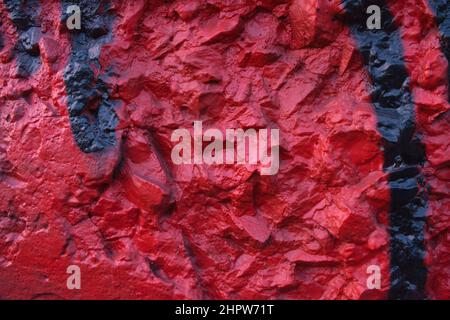 Dark red painted relief wall with rough chaotic convex elements. Concrete wall covered uneven decorative stucco and painted dark red and black paint.  Stock Photo
