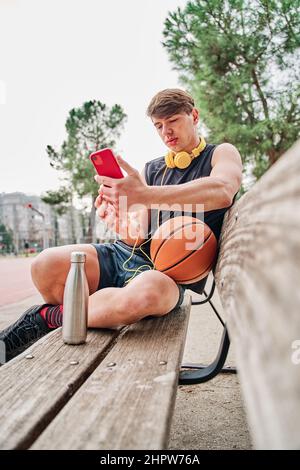 basketball player resting. male athlete sitting while making a video call on his mobile phone. Stock Photo