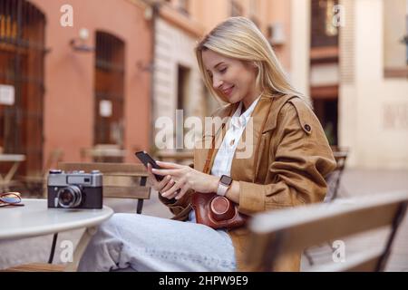 Side photo of happy female holding smartphone and sitting at table Stock Photo