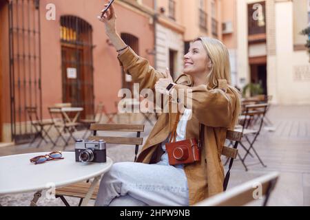 Woman taking selfie on smartphone sitting outside Stock Photo