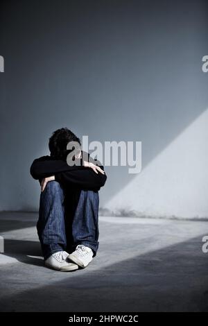 Hes feeling really sad. A young man sitting on the ground and resting his head on his folded arms. Stock Photo