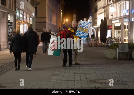 Munich, Germany. 23rd Feb, 2022. Participants with Bavaria flag and Wales flag. On February 23, 2022, hundreds of anti-vaxxers gathered to demonstrate against mandatory vaccination and covid protection measures. They lined up between the Geschwister-Scholl-Platz and Odeonsplatz to form a chain of lights. The mask obligation and distance rules were hardly kept. (Photo by Alexander Pohl/Sipa USA) Credit: Sipa USA/Alamy Live News Stock Photo