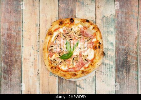 Pizza with slices of cooked ham, mozzarella cheese and mushroom slices with an aromatic basil leaf in the center Stock Photo