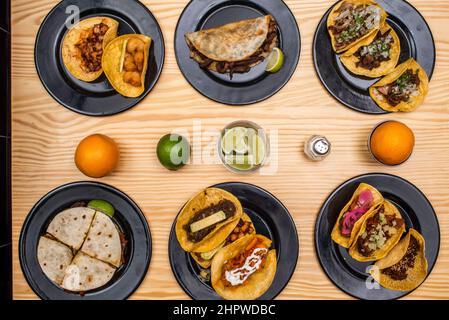 Image of a set of typical Mexican cuisine dishes with chickpea tacos, gringas, quesadillas and whole and chopped limes along with oranges and salt sha Stock Photo